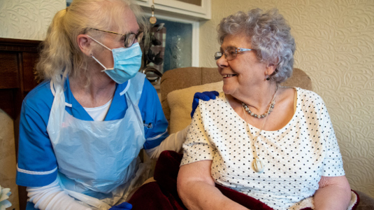 Carer in full PPE sitting with client in her home