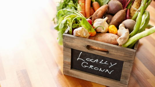 A box of fresh vegetables with the words locally grown written on the front of the box