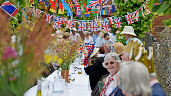 Street Party with people at a long table dressed with flowers and bunting, enjoying food and drink