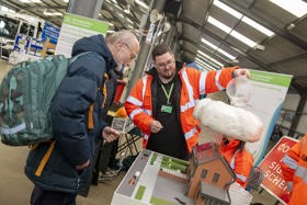 A member of the flooding team in an orange High Vis jacket demonstrates the effect of rain on flooding to a visitor at the county show. He is pouring water through a model cloud on to the roof of a model house
