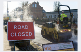 Via roadworker on a rolling machine to flatten out the new road surface. There is a Via works notice in the foreground and a Road Closed red sign to show the road is closed while it is being worked on