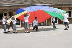 Children playing with colourful parachute in school playground