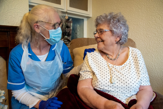 Carer in full PPE sitting with client in her home