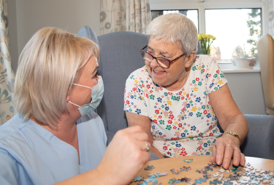 Carer in PPE doing a jigsaw with a lady in a care home