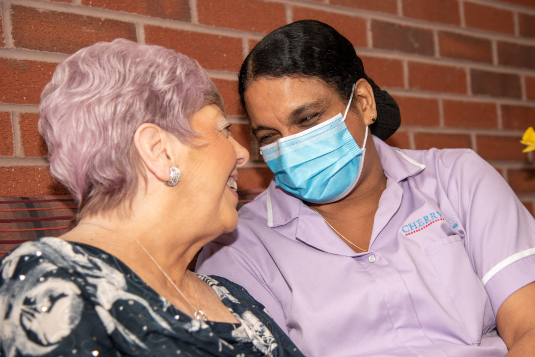 Carer in PPE sat beside a lady smiling at each other