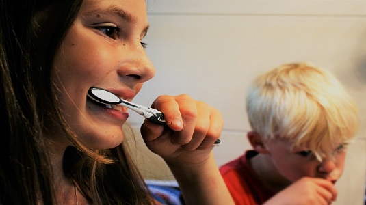 A girl and a young boy brushing their teeth