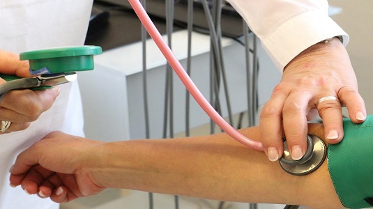 A person performing a health check on another person with a medical device placed on the inner arm