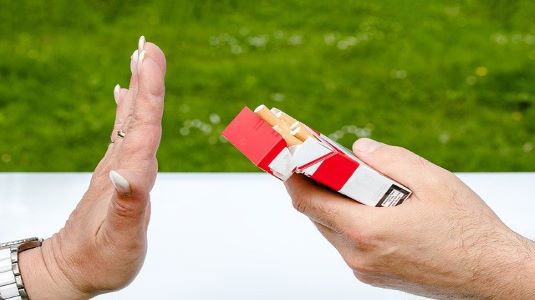 A hand held up refusing to take a cigarette from an offered packet