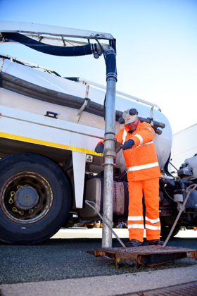 A man in orange hi-vis undertaking a gully clearance with a maintenance vehicle in the background