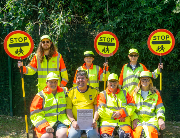 Seven crossing guards, six in uniform, with their lollipops and a certificate for 70 years of crossing guards