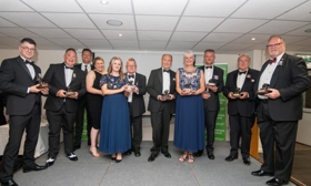 A picture of people standing in front of a wall, holding trophies.
