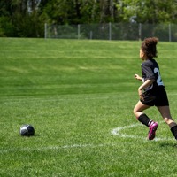 A young girl dressed in a football kit running towards a ball in a field.