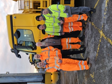 A shot of Cllr Bert Bingham (Left) with five members of the gritting team standing in front of a gritter