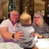 Foster carers Ruth and Phil sat at a table with a small child. They are smiling.